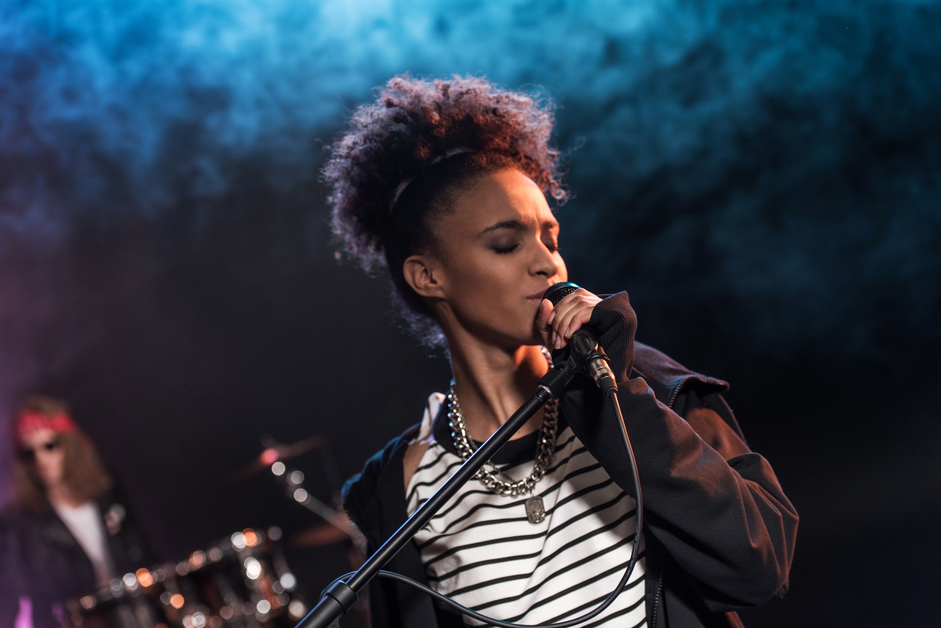 Female singer with microphone and rock and roll band performing hard rock music on stage