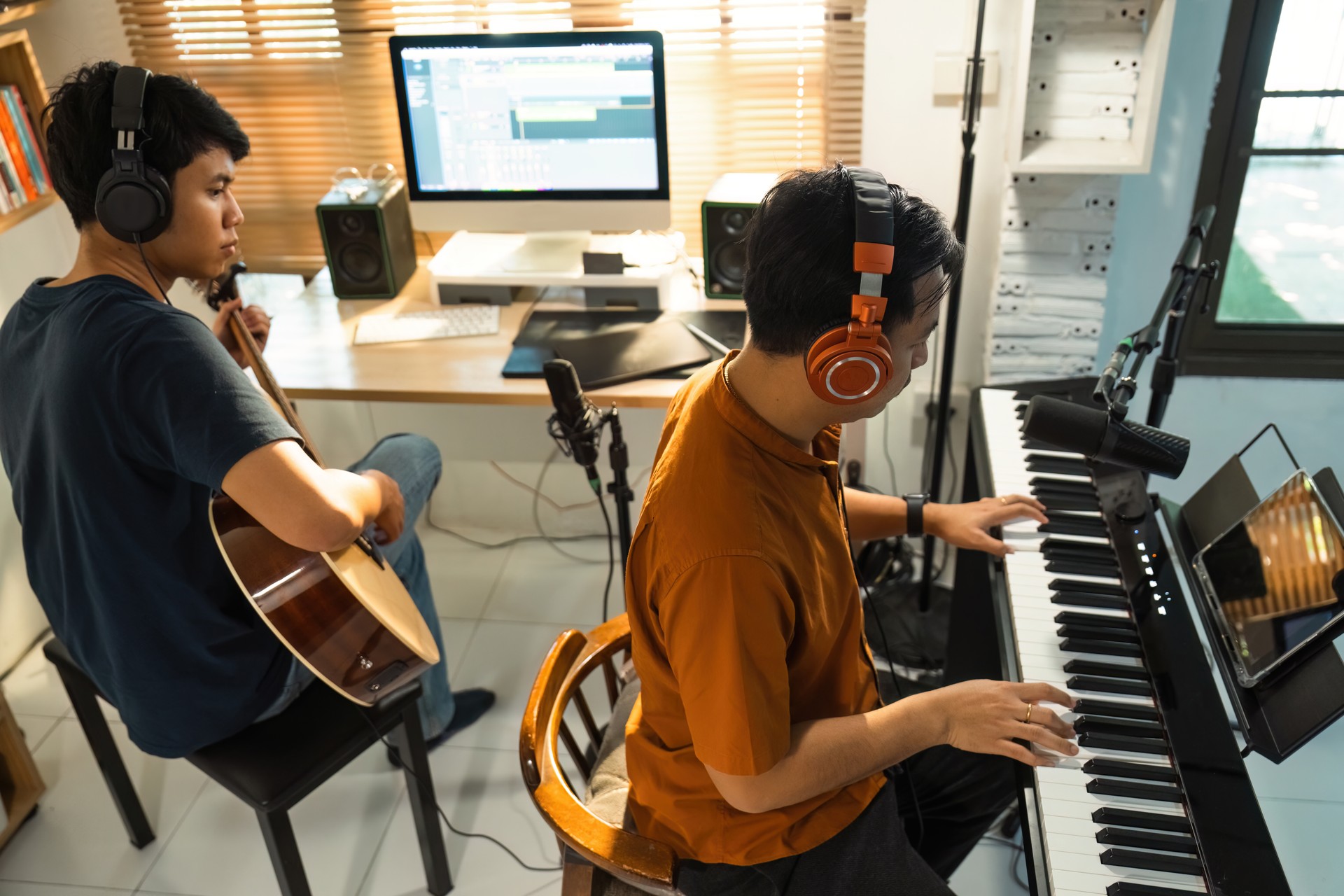 Group of Asian men making music at home studio. He plays guitar and keyboard.